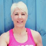 Helen Wood, a fitness professional, smiling in a pink workout top against a blue wooden background in Tynemouth.